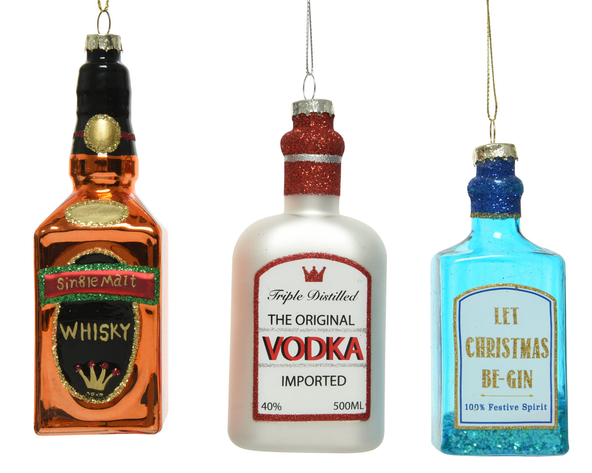 Three Christmas tree ornaments shaped like liquor bottles hanging side by side on a white background: an amber whiskey bottle, a white vodka bottle, and a blue gin bottle with festive labels.