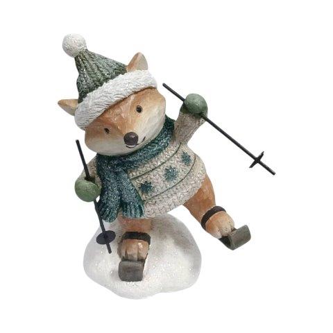 A decorative figurine of a fox dressed in winter ski clothing, including a green knit hat with white trim, a green knit scarf, and a matching knit sweater, posed on a snowy base with ski poles.