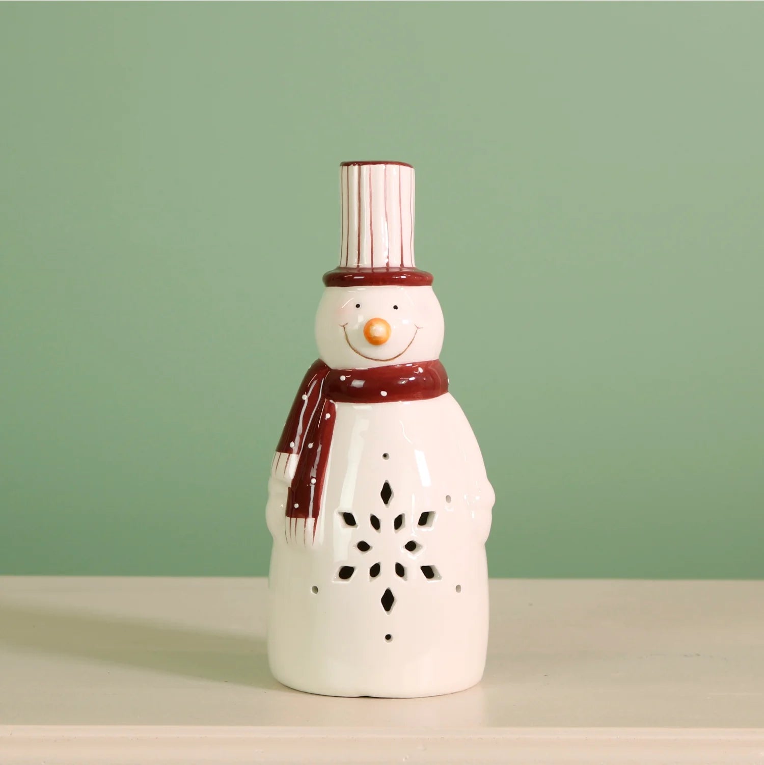 Ceramic snowman ,white and red with star cut out on a green background. Christmas Light