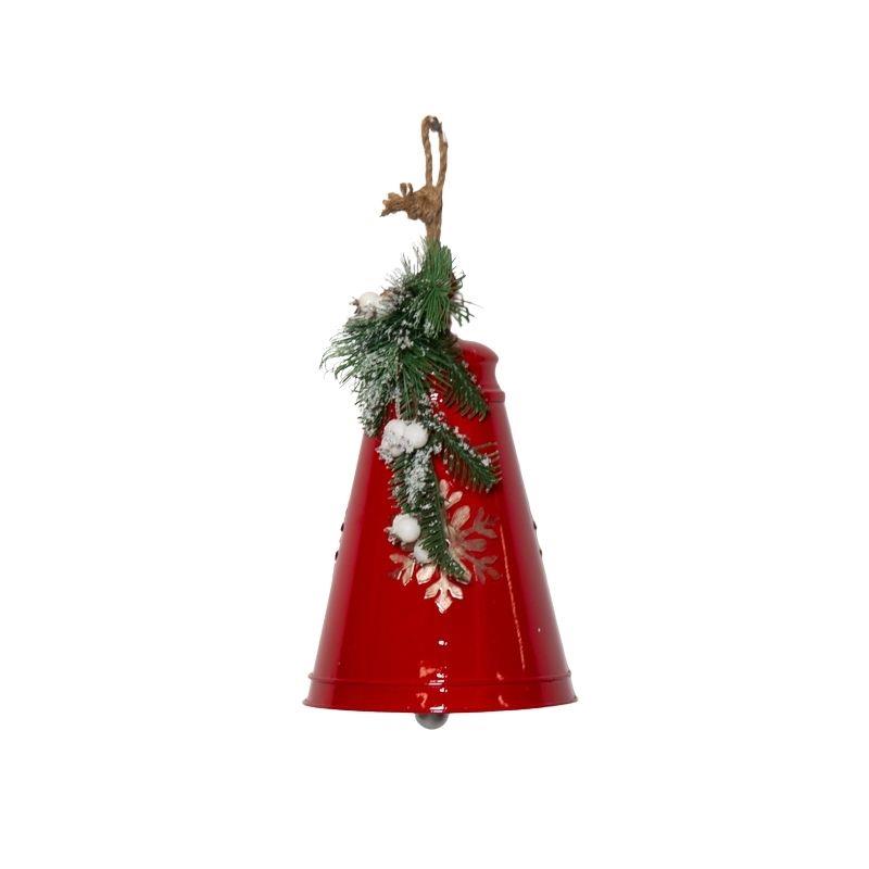 A red metal bell-shaped Christmas ornament decorated with green pine branches, white faux snow, and a small reindeer hanging from a brown string, shown on a plain white background.