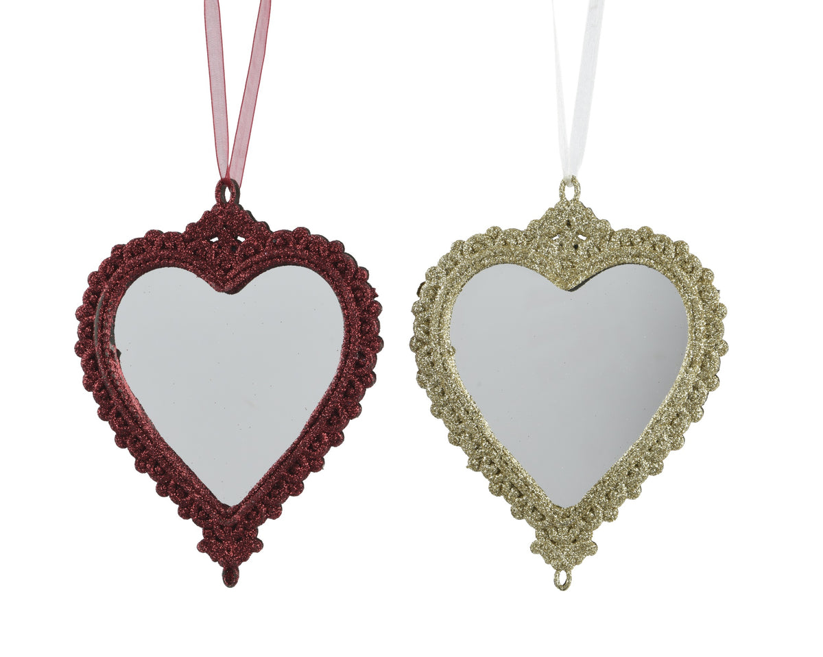 Two heart-shaped hanging ornaments with ornate scalloped edges and mirrored centers, shown side by side on a white background. One ornament is dark red with a pink ribbon, and the other is gold with a white ribbon.