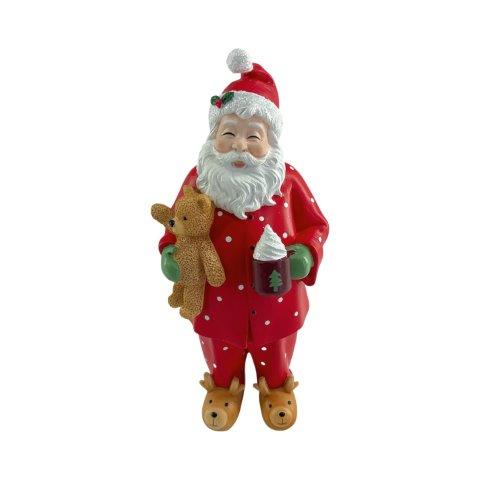 A Santa Claus figurine wearing a red suit with white polka dots, a red hat with a white pom-pom, a white beard, green gloves, and brown reindeer slippers, holding a teddy bear and a mug of hot chocolate against a plain white background.