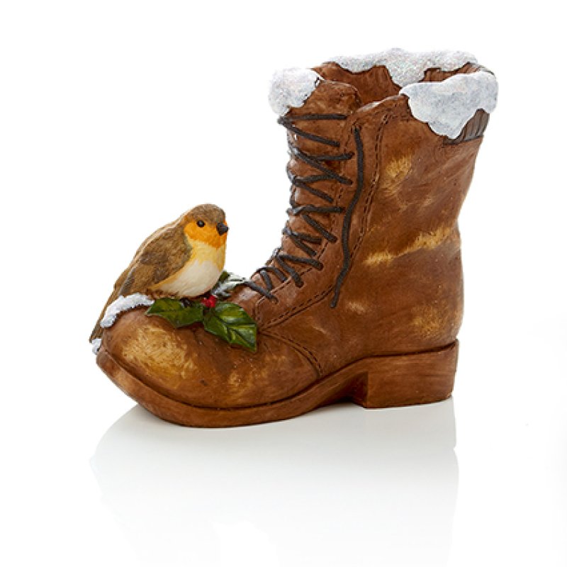 A Christmas ornament shaped like a brown leather boot with faux snow on the trim, a small robin bird perched on the toe area, and green holly leaves, shown on a white background.